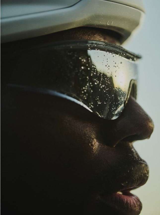 Close-up profile shot of a dark-skinned adult wearing a white helmet and protective eyewear, highlighting the water droplets on the lenses.