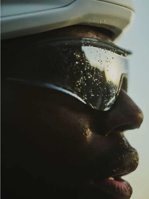 Close-up profile shot of a dark-skinned adult wearing a white helmet and protective eyewear, highlighting the water droplets on the lenses.