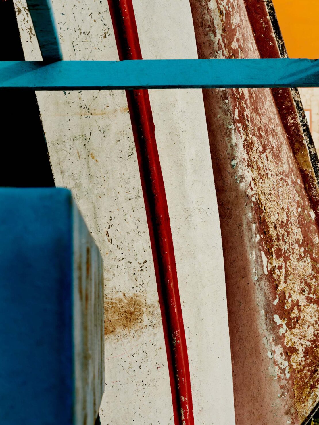 Abstract image of weathered boat hull with red and white paint, accented by turquoise structural elements. Bright light.