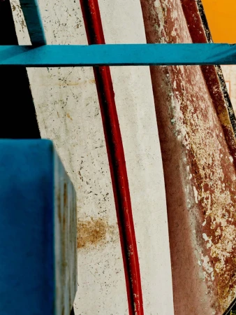 Abstract image of weathered boat hull with red and white paint, accented by turquoise structural elements. Bright light.