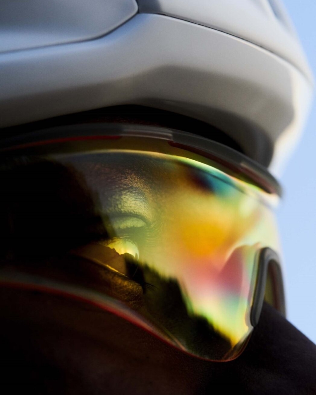Close-up of cyclist wearing helmet and mirrored sports glasses, reflecting the sky, suggesting outdoor cycling and sports.