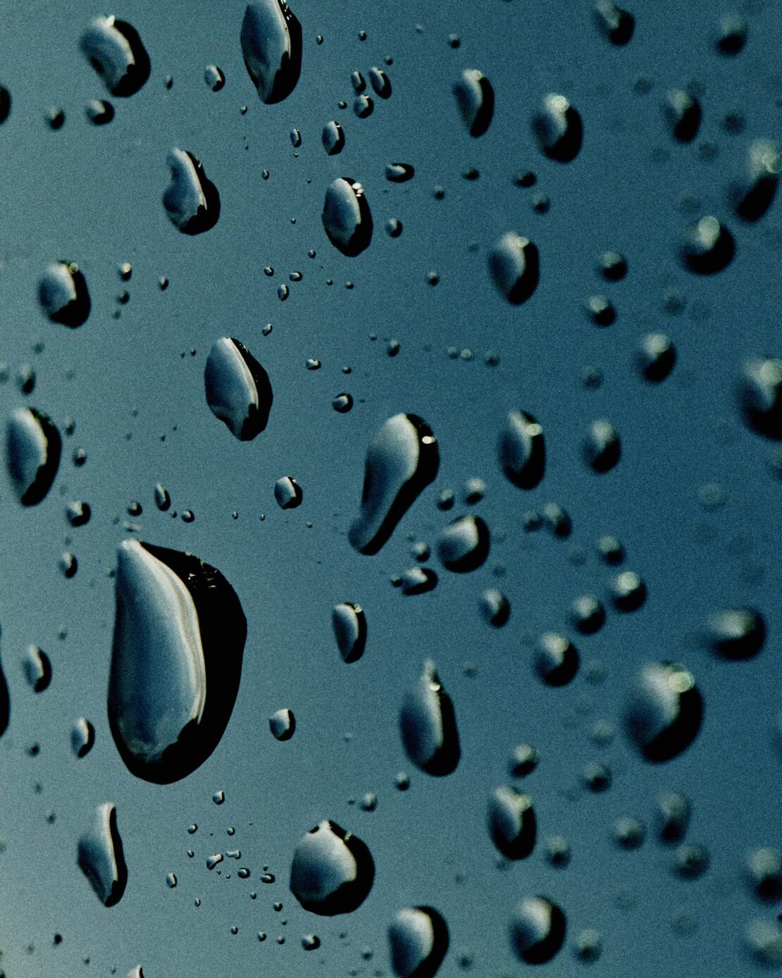 Close-up of water droplets on a teal surface, creating a textured pattern with reflections and abstract shapes on a wet surface.