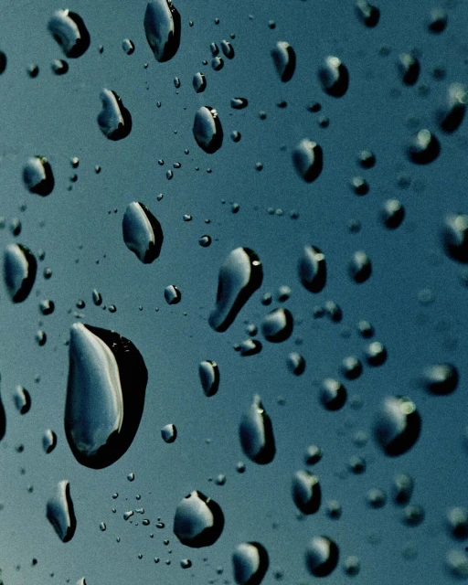Close-up of water droplets on a teal surface, creating a textured pattern with reflections and abstract shapes on a wet surface.