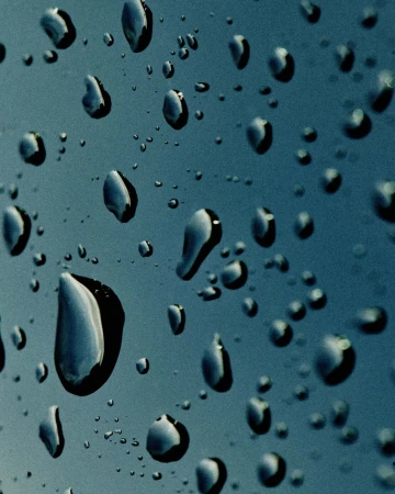 Close-up of water droplets on a teal surface, creating a textured pattern with reflections and abstract shapes on a wet surface.