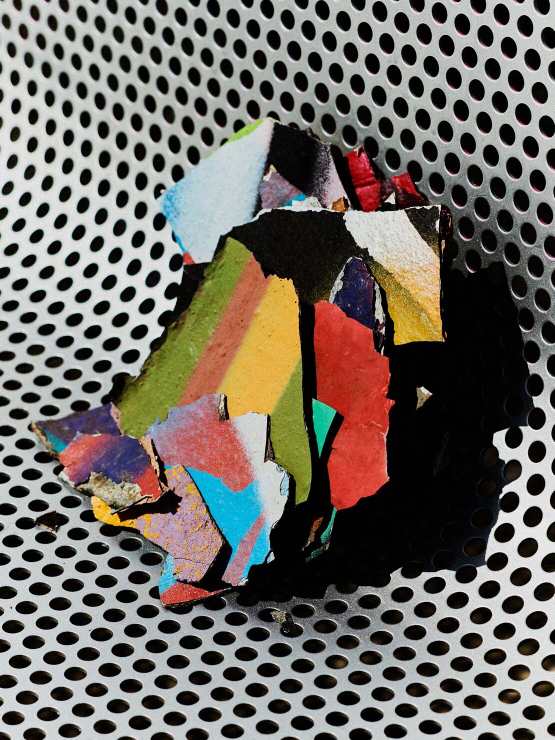 Abstract art: a fragment of painted debris with vibrant colors lies on a perforated silver metal surface, creating a textured contrast.