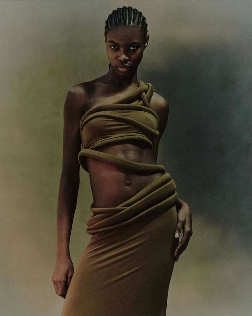 Fashion shot of an adult African-American woman wearing a draped olive green dress looking at the camera in a studio with soft lighting.