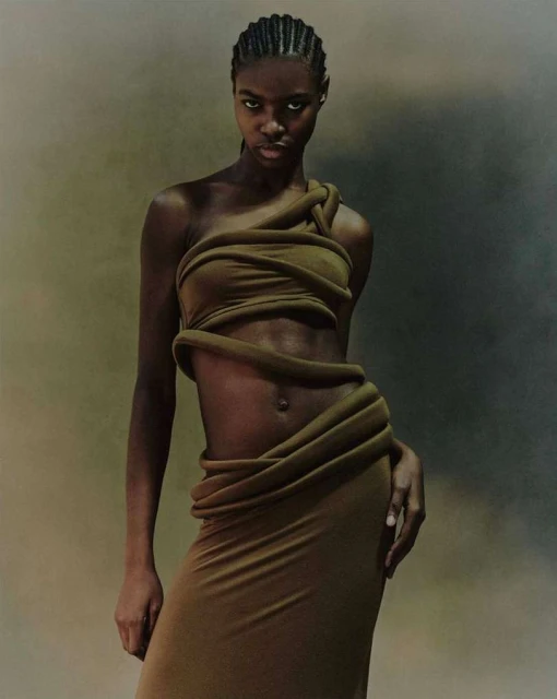 Fashion shot of an adult African-American woman wearing a draped olive green dress looking at the camera in a studio with soft lighting.
