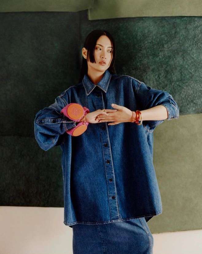Asian woman wearing an oversized denim shirt holding pink wrist accessories, photographed by Daniel Benson in London.