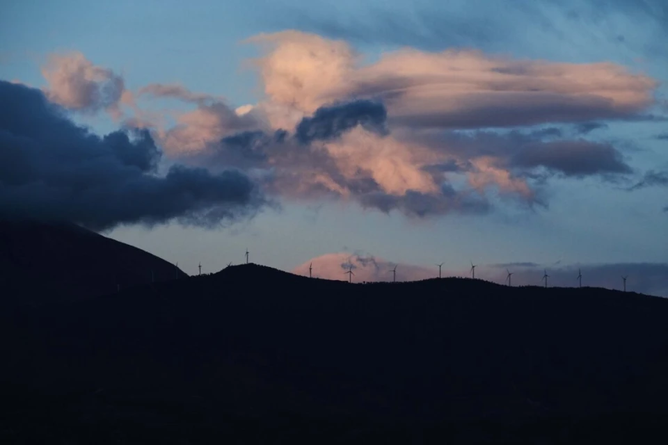 Wind turbines on a mountain ridge at dusk with pink and blue clouds filling the sky, creating a scenic landscape view.