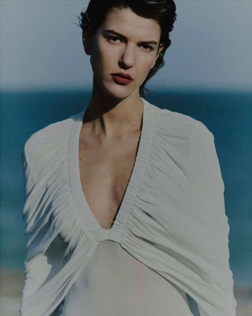 Portrait of a woman wearing a white V-neck top outdoors with a blurred ocean background by Daniel Benson