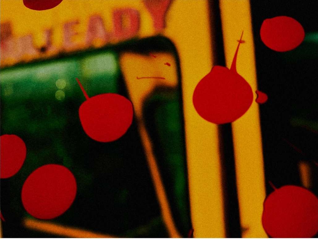 Abstract close-up of red droplets against a blurred background with yellow and green tones and indistinct text, creating an artistic effect.