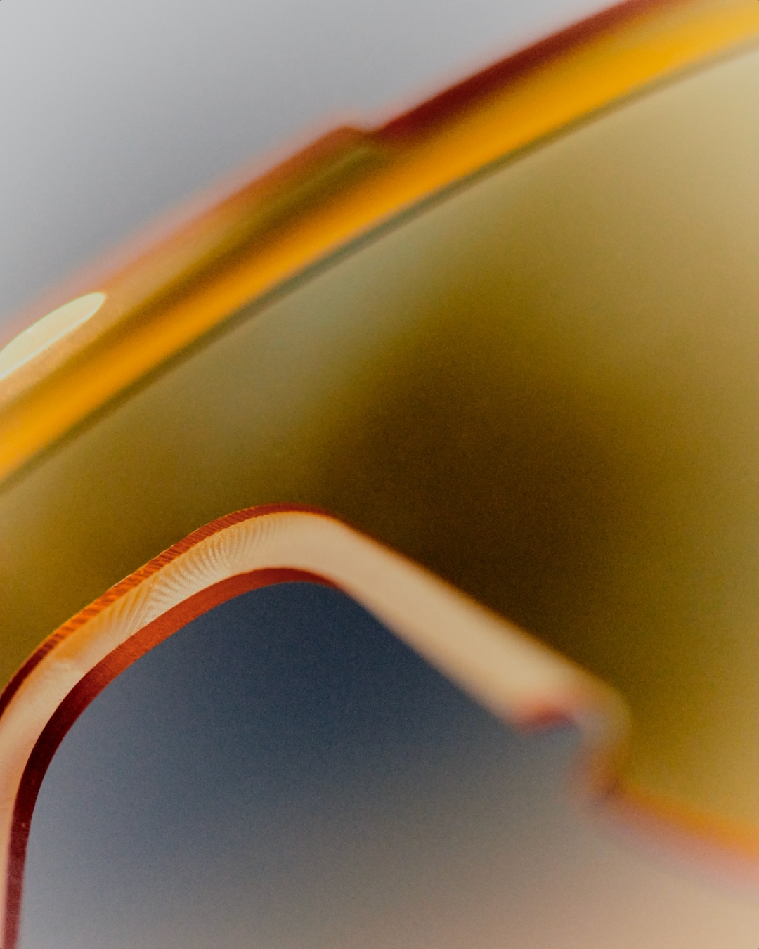 Macro shot of the tinted lens and frame of sunglasses. The warm hues and blurred edges create a sense of mystery and high fashion.