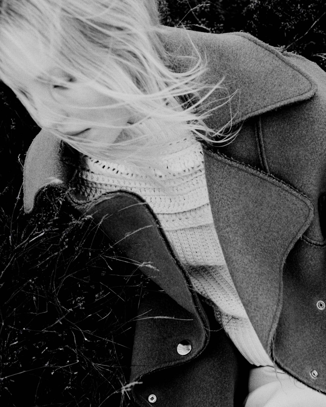 Overhead shot of a fair-skinned adult female model with blonde hair wearing a wool jacket and knitted sweater outdoors.