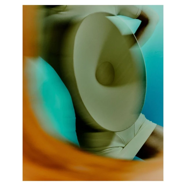 Abstract fashion shot featuring a person in a tan outfit behind a circular object with blurred orange and blue background.
