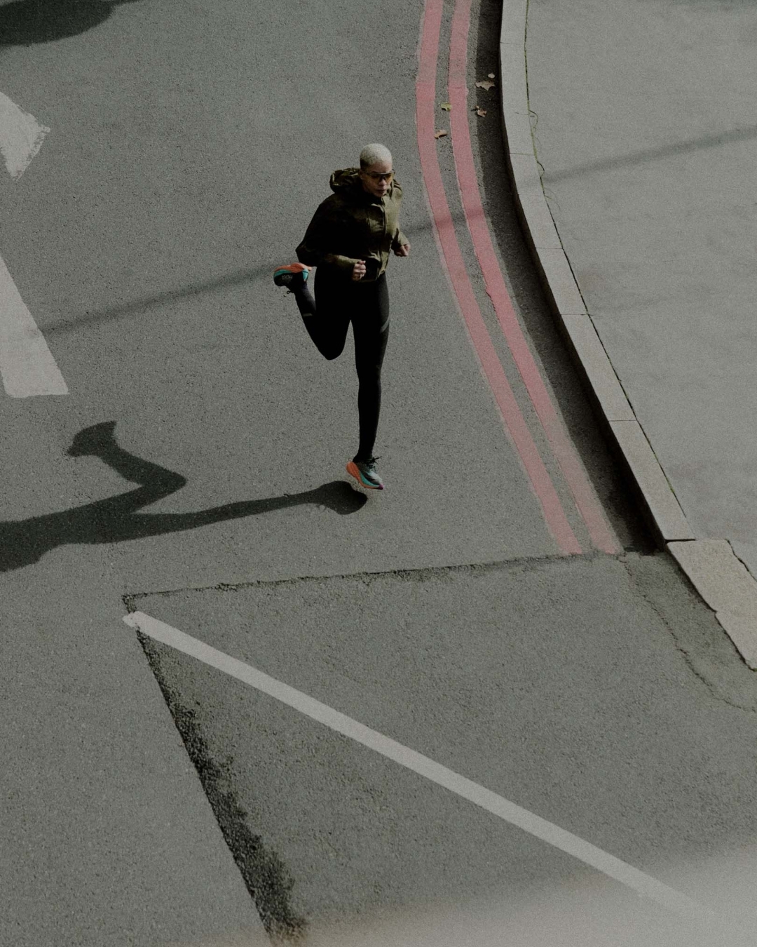 Adult female athlete stretches her leg on an urban street with grey asphalt and pink lines, creating a dynamic fitness scene.