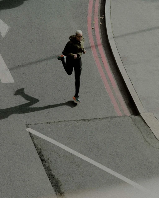 Adult female athlete stretches her leg on an urban street with grey asphalt and pink lines, creating a dynamic fitness scene.