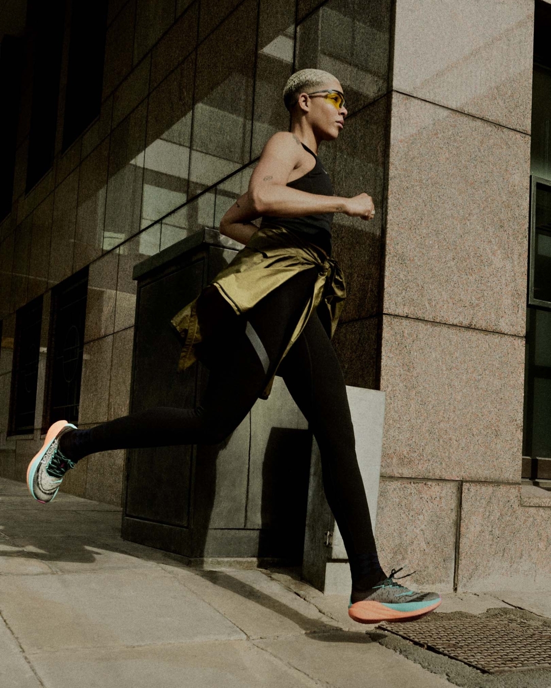 Runner in black leggings and tied jacket running past urban stone building exterior in London