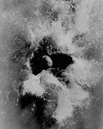 Monochrome image of an egg-shaped object in a dark void, encircled by a burst of splashing water, evoking a cosmic scene.