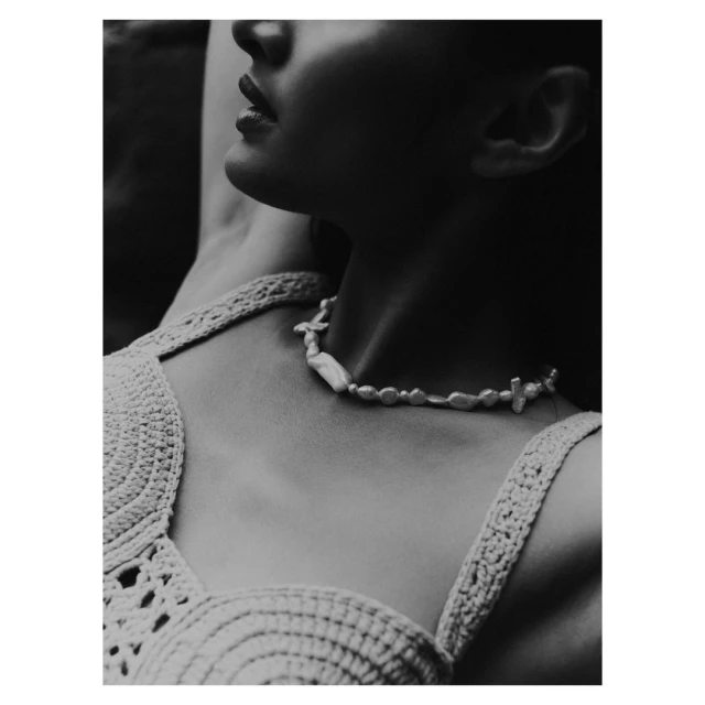 Monochrome portrait of a woman with a pearl necklace, wearing a crochet top, photographed in soft lighting, evoking natural beauty.