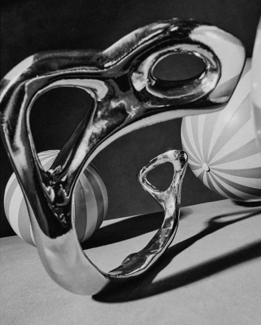 Monochromatic photograph of a polished metal sculpture featuring a smooth, rounded design with striped spheres in the background.