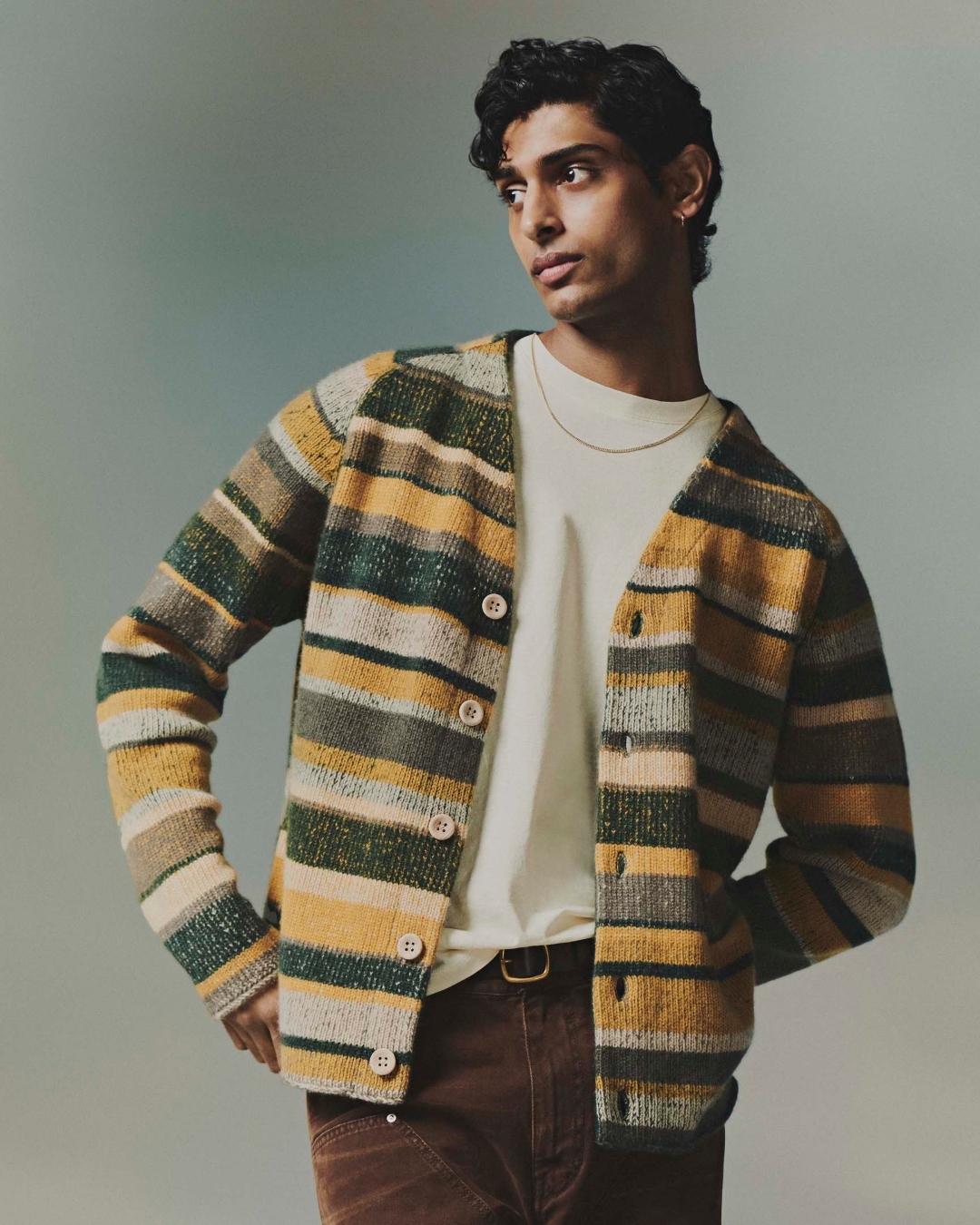 Man wearing a striped cardigan and white t-shirt against a grey studio backdrop