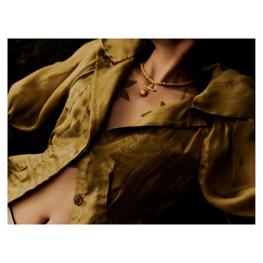 Woman in a gold satin blouse and gold necklace with a round pendant lying in a dark setting. Beauty, fashion, and jewelry.