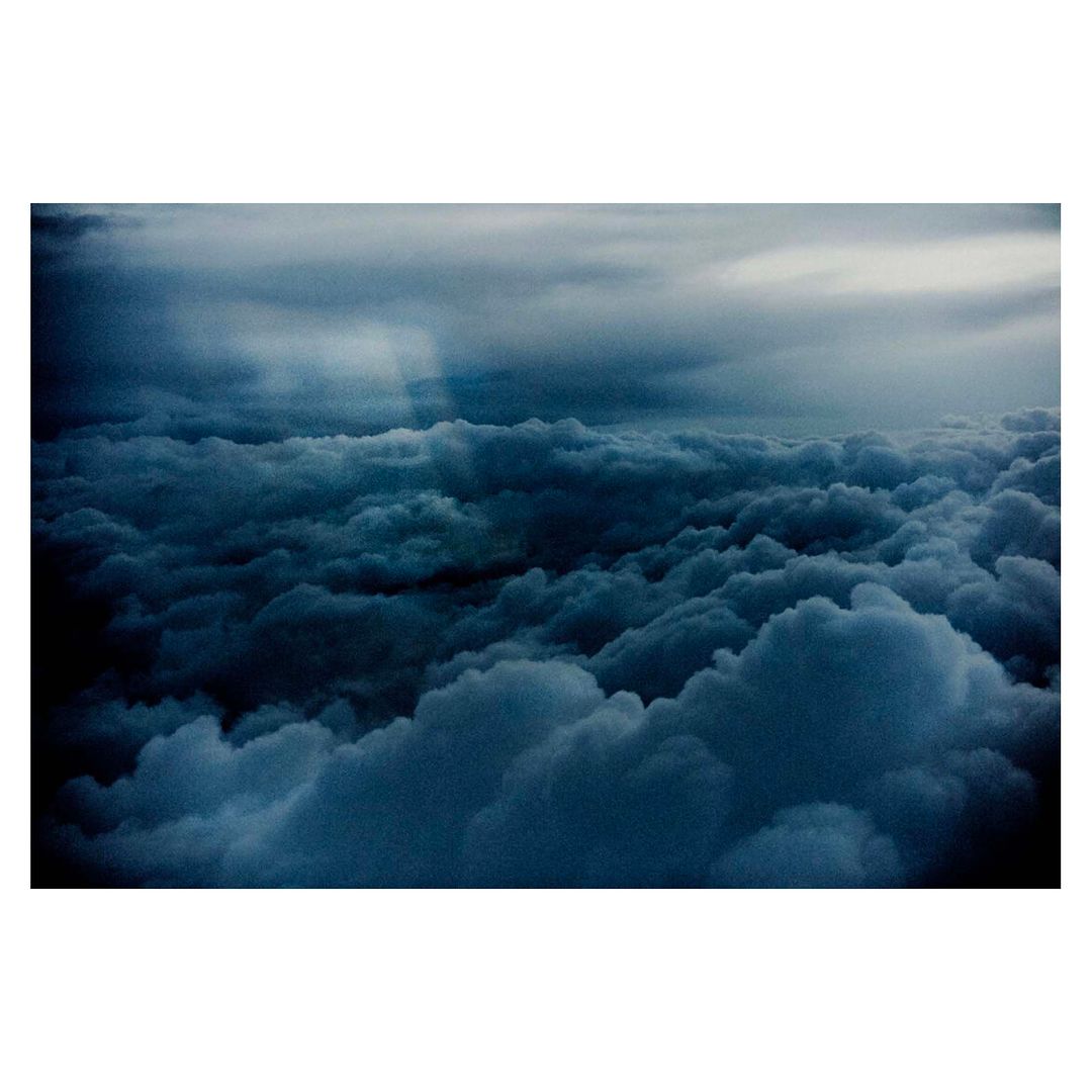 Dramatic aerial view of dark, densely packed storm clouds with crepuscular rays peeking through the cloud cover, creating a moody atmosphere.
