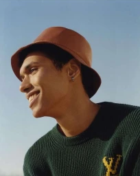 Close-up portrait of smiling young man wearing brown bucket hat and green knit sweater against clear blue sky by Daniel Benson