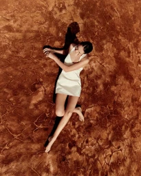 Aerial view of a woman in a white slip dress lying on cracked red earth by Daniel Benson
