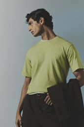 Portrait of a man in a green t-shirt holding a dark jacket against a light blue gradient backdrop.