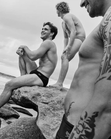 Black and white portrait of three men in swimwear posing on rocky coastal rocks by Daniel Benson in London.
