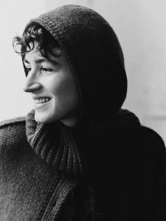 Black and white portrait of a smiling person wearing a dark hooded knit sweater in London by Daniel Benson.