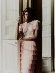 Woman in pale pink tiered tulle dress standing by an open white paneled door with natural light.