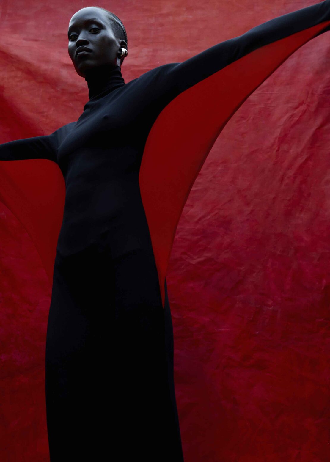 Elegant Black Woman in Black Dress Against Red Backdrop. Striking studio shot with a model in fashionable attire.