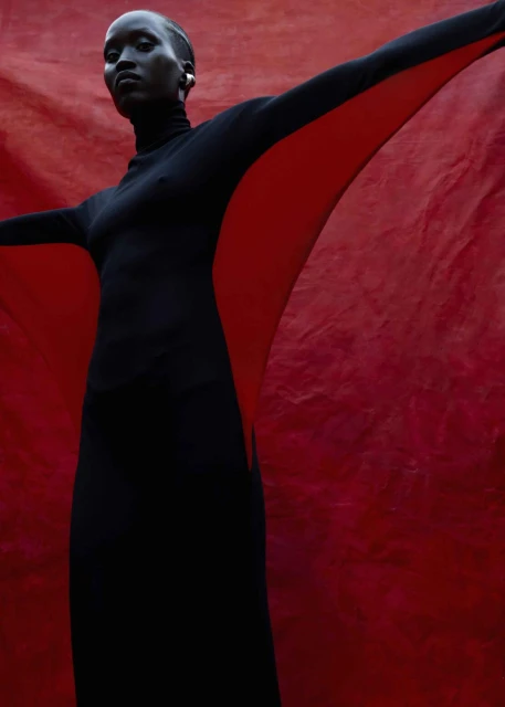 Elegant Black Woman in Black Dress Against Red Backdrop. Striking studio shot with a model in fashionable attire.