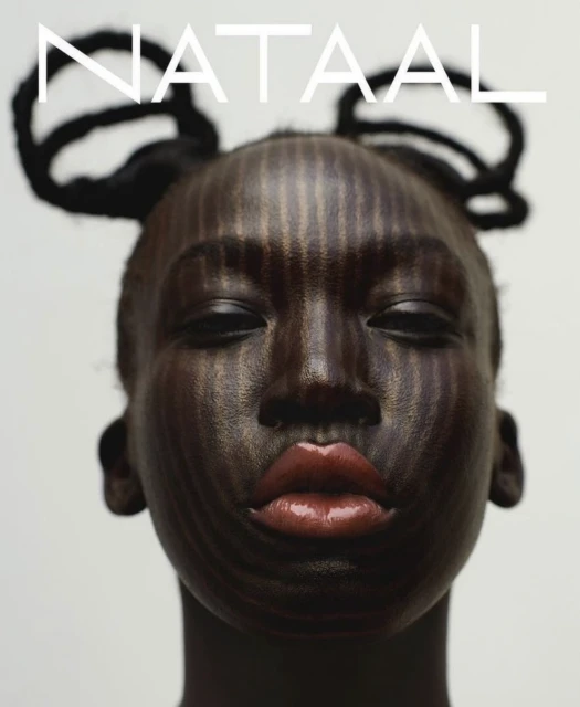 Close-up portrait of a woman with dark skin and intricate makeup featuring vertical stripes, accented by unique hairstyle and bold red lips.
