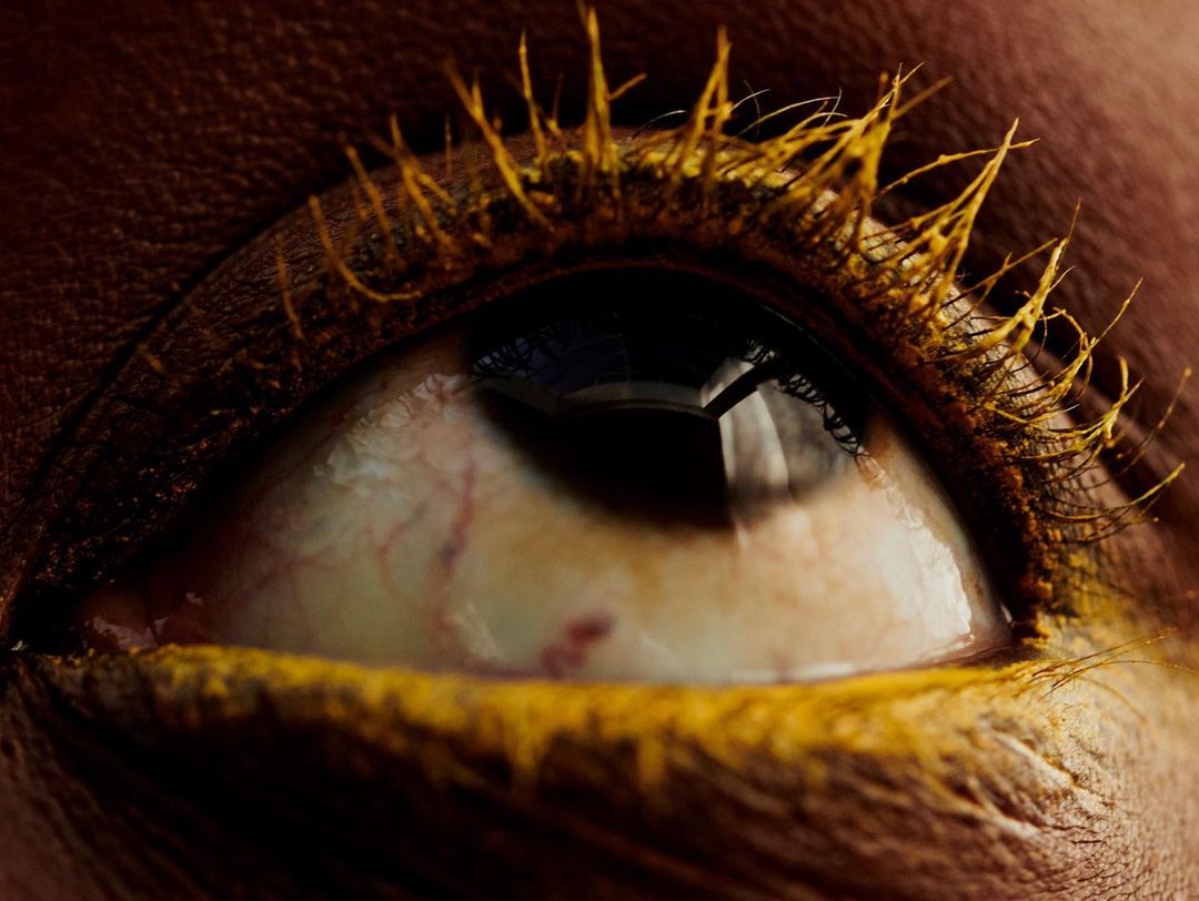 Macro close-up of a human eye with golden-yellow color cosmetic makeup around the eye, including the lashes and lower lid.