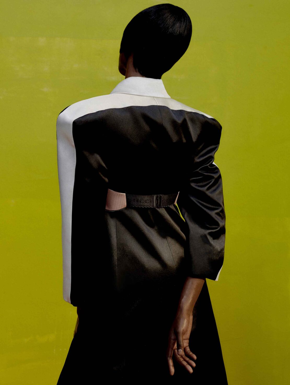 Back view of a Black model in a black and white dress against a yellow background. Fashion editorial style photograph.