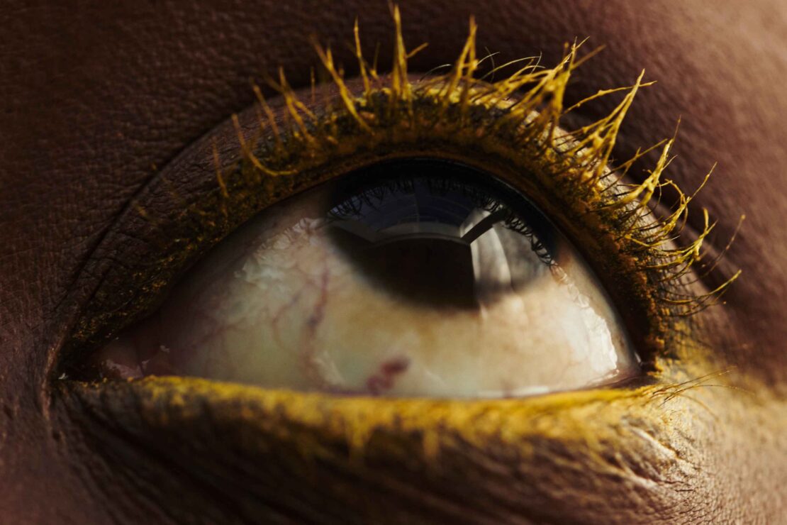 Macro close-up of a human eye with yellow makeup on the eyelashes and around the eye, showcasing beauty and cosmetic artistry.