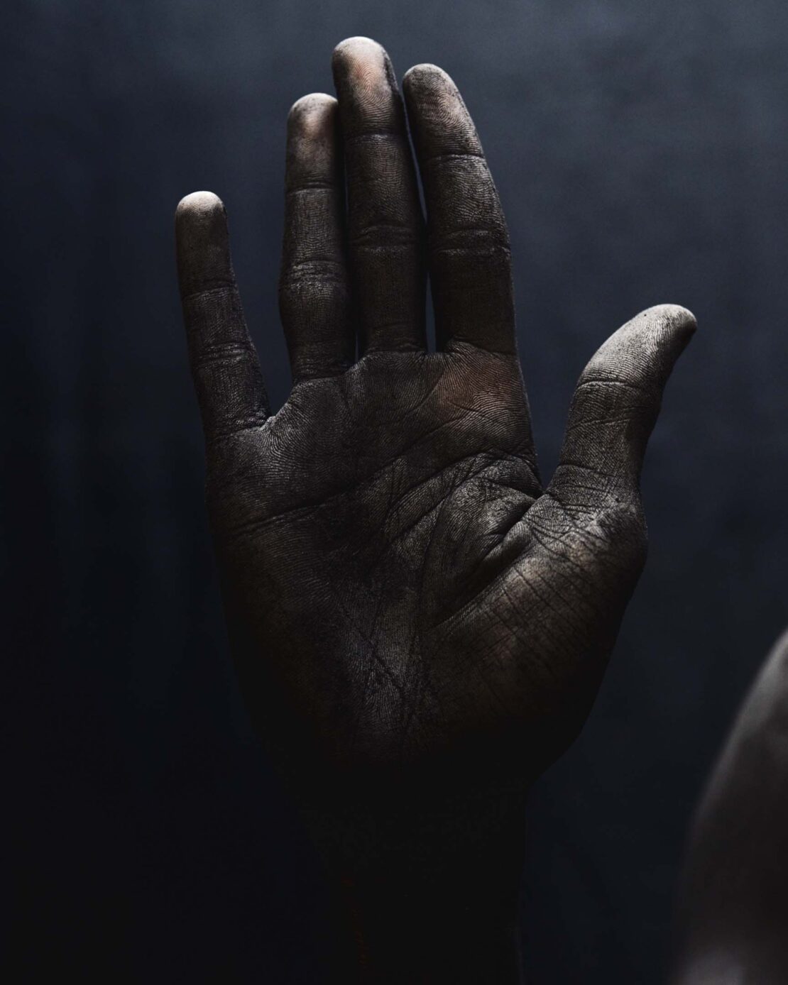 Close-up studio shot of a dirty adult hand, fingers extended against a dark background, showcasing texture and detail with chiaroscuro lighting.