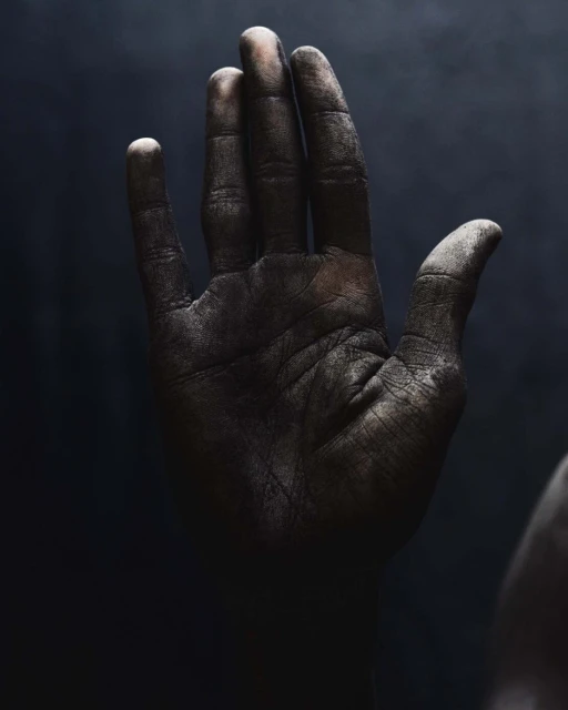 Close-up studio shot of a dirty adult hand, fingers extended against a dark background, showcasing texture and detail with chiaroscuro lighting.