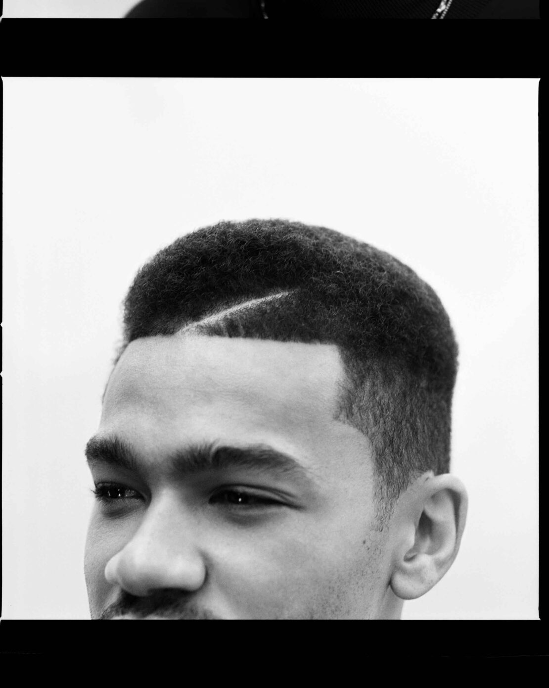 Close-up portrait of a Black man with short textured hair and a distinct parting line, captured in monochrome by Ekua King.