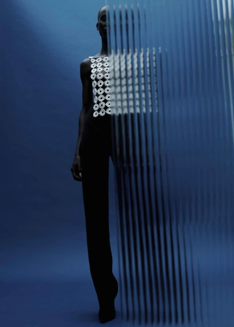 Artistic fashion shot featuring an adult woman in a white top and dark pants, posing behind a linear semi-transparent screen against a blue backdrop.