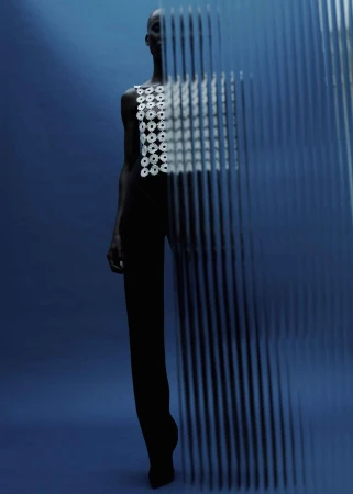Artistic fashion shot featuring an adult woman in a white top and dark pants, posing behind a linear semi-transparent screen against a blue backdrop.