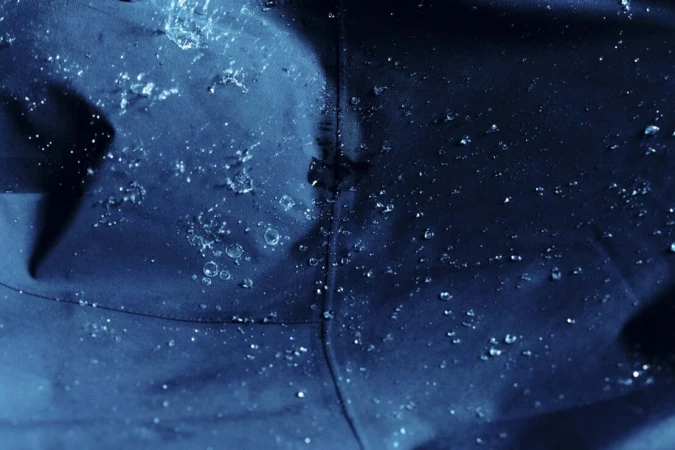 Close-up of water droplets beading on a dark blue waterproof fabric surface with a visible stitched seam.