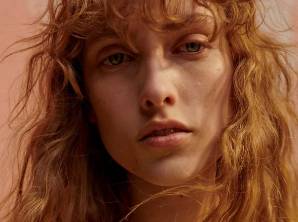 Close-up portrait of a woman with long curly hair and light eyes, captured in warm lighting by photographer Ekua King.