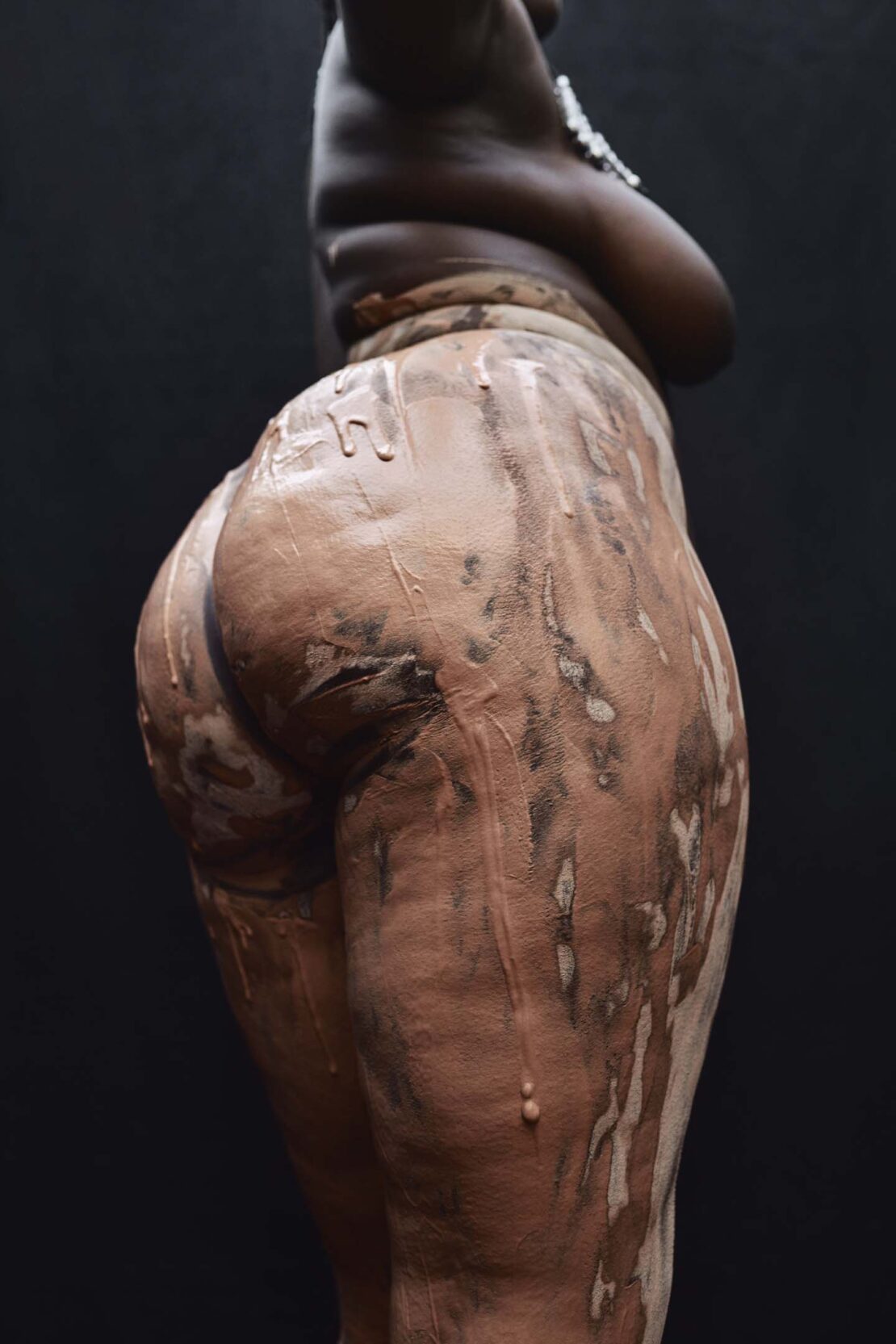 Close-up portrait of a black woman covered in clay against a dark background, photographed by Ekua King.