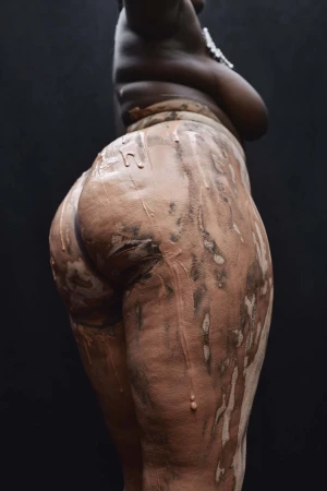 Close-up portrait of a black woman covered in clay against a dark background, photographed by Ekua King.