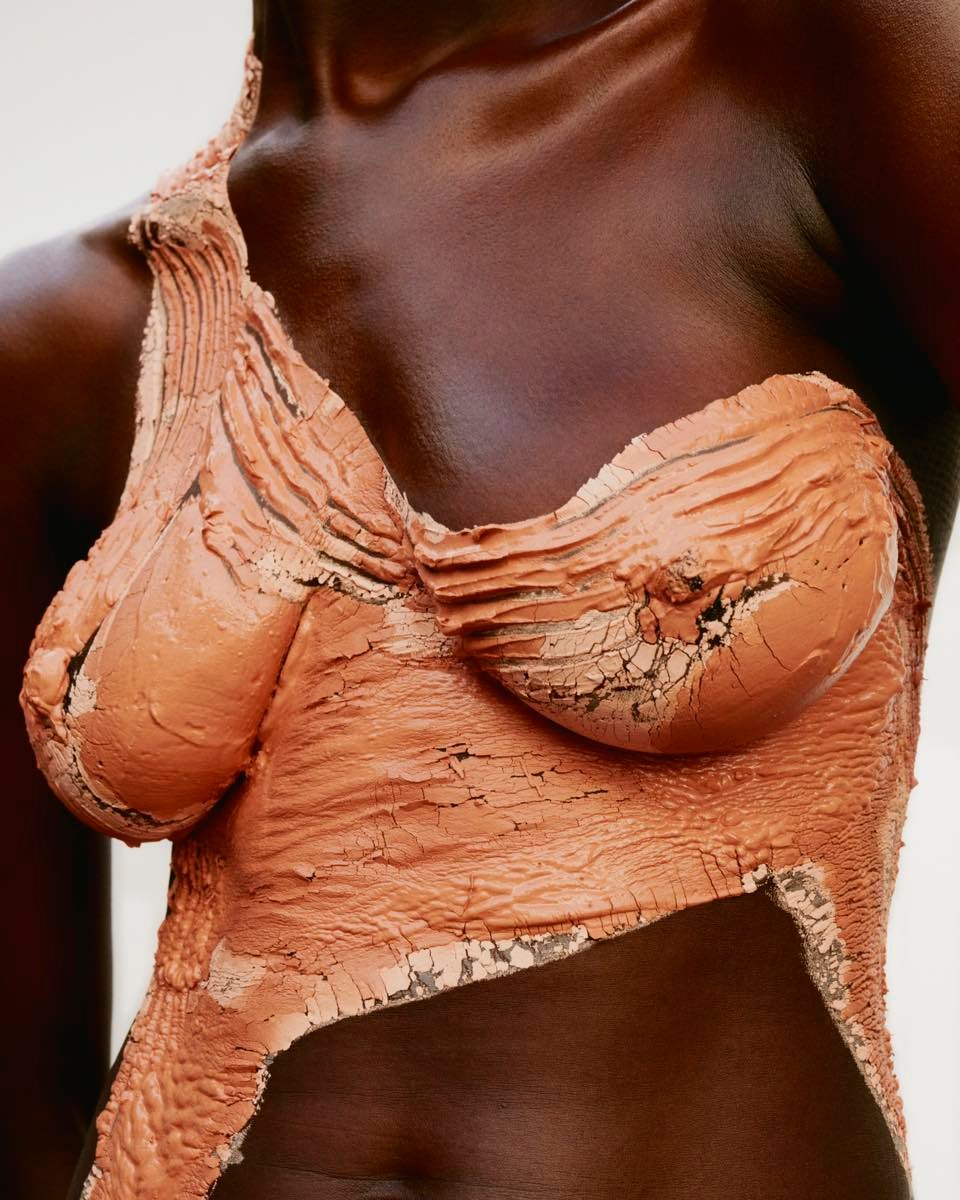 Close-up of a Black woman with clay-like body paint, showcasing body art, beauty concept, skin tone, and neutral studio background.