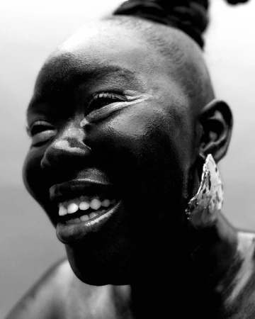 Close-up black and white portrait of a smiling Black woman wearing a large textured earring and her hair in a high bun.